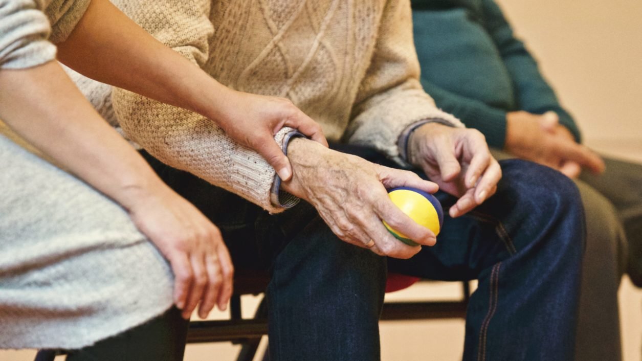 An elderly person holding a ball with a care provider supporting them