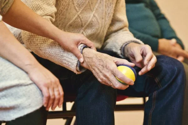 An elderly person holding a ball with a care provider supporting them