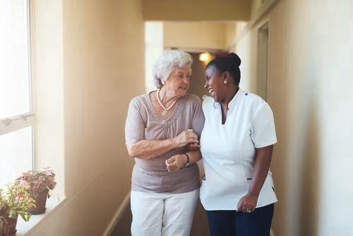 An elderly women and a care provider walking down a hallway together laughing