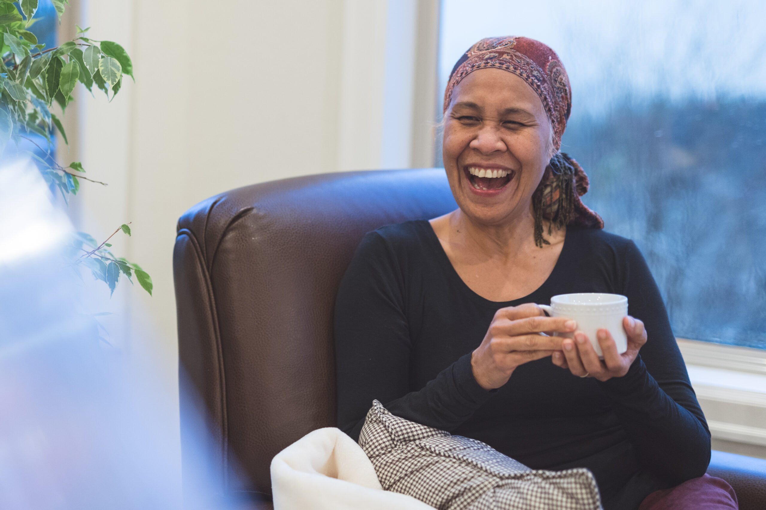 Senior woman with cancer laughing in an armchair holding tea