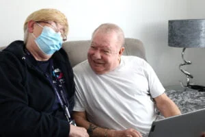 An Abbots Care visiting care worker sitting on a sofa with a care service user laughing together
