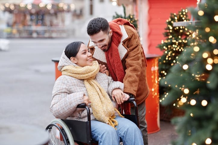 Couple at Christmas time, the lady is in a wheelchair whilst her partner is standing next to her